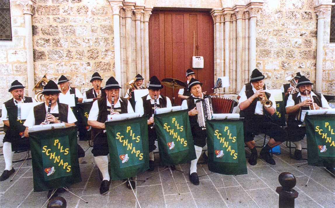 Nous jouons en formation devant le porche d’une église, pupitres ornés de nos fanions Pils-Schnaps